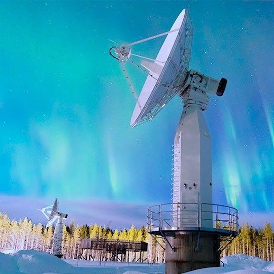 Two remote sensing antennas mounted in a snowy field pointed at a beautiful, blue streaky sky