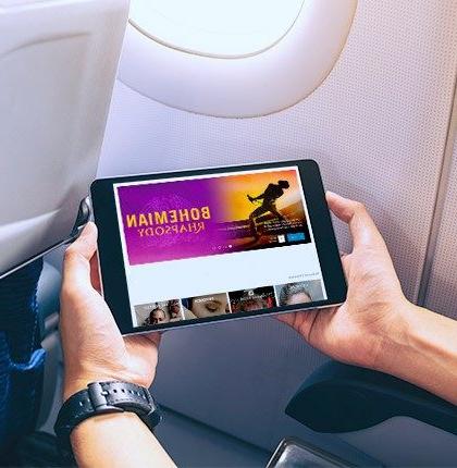 Close-up of hands holding a small tablet showing Bohemian Rhapsody, connected to inflight technology