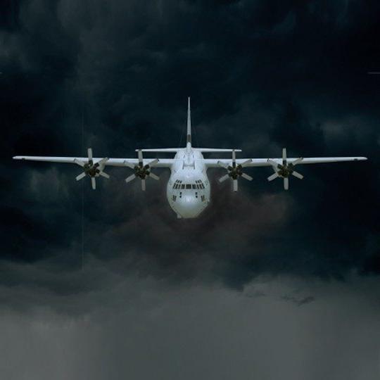 Front view of a C-130J aircraft flying through dark clouds