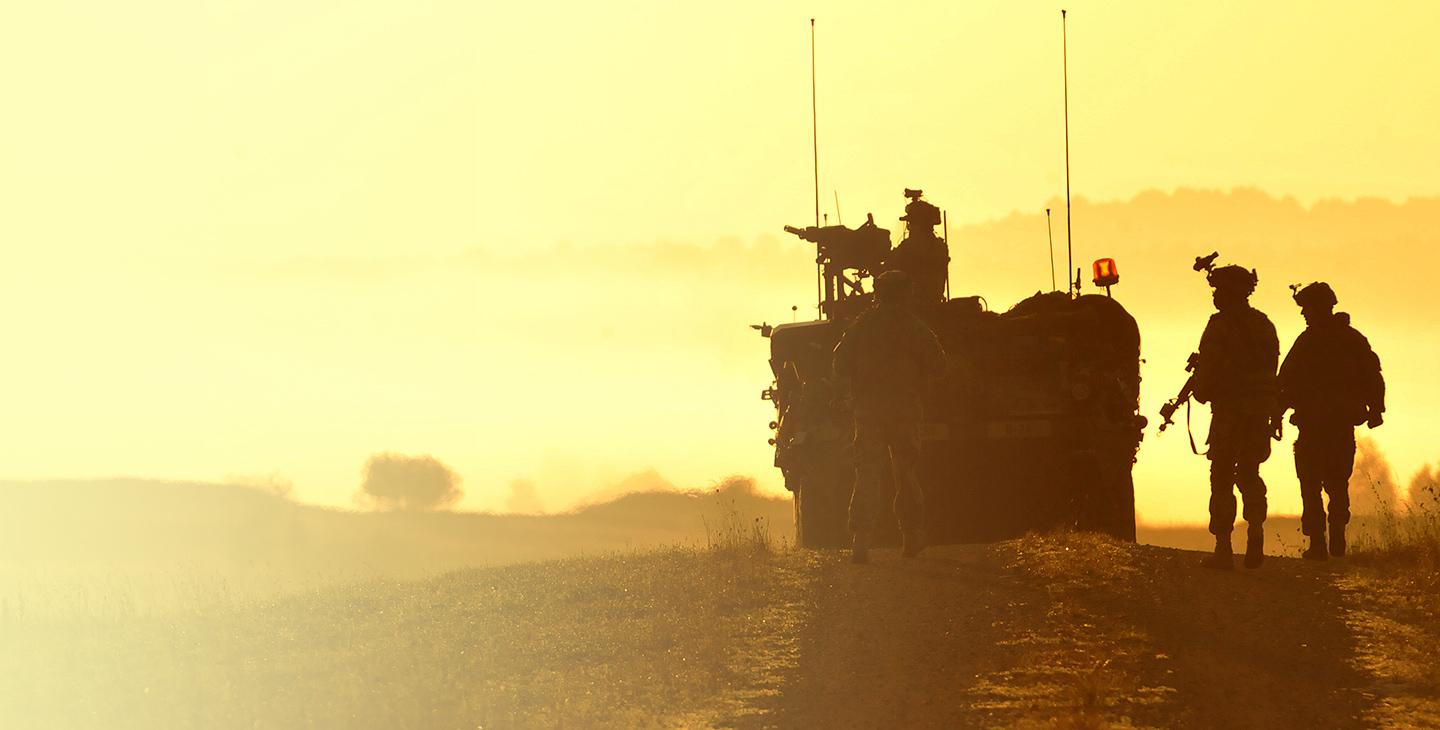 Four soldiers at dusk with a military vehicle utilizing mobile integrated solutions for tactical operations