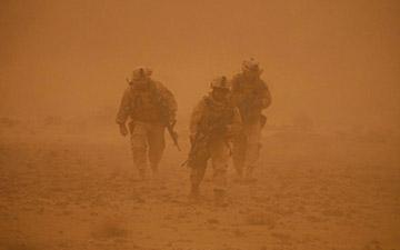 Three soldiers walking through a sand storm
