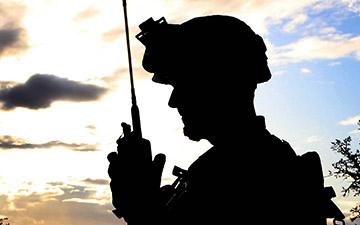 Silhouette of a soldier talking on a handheld radio at disk